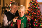 a picture of Senior Citizen . Adult . Christmas . Couple . Holiday . Indoor . Interior . Light . Man . Mature Adult . People . Person . Portrait . Relationship . Senior Citizen . Tree . Woman . Bonding . Festive . Smile . Togetherness . Candle . Decoration . Standing . Female . Male . People 2 . Husband . Wife . Matches . Flame . Age 60s . Horizontal . Caucasian .